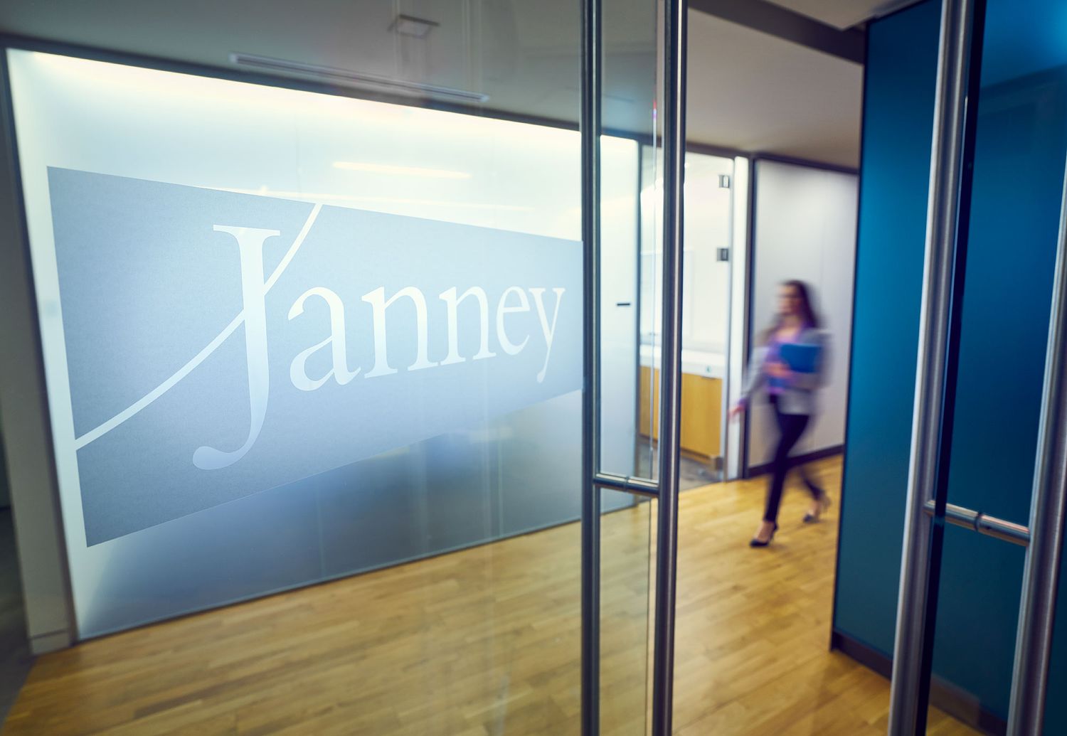 Glass office entrance with frosted Janney logo and blurred professional walking in background.
