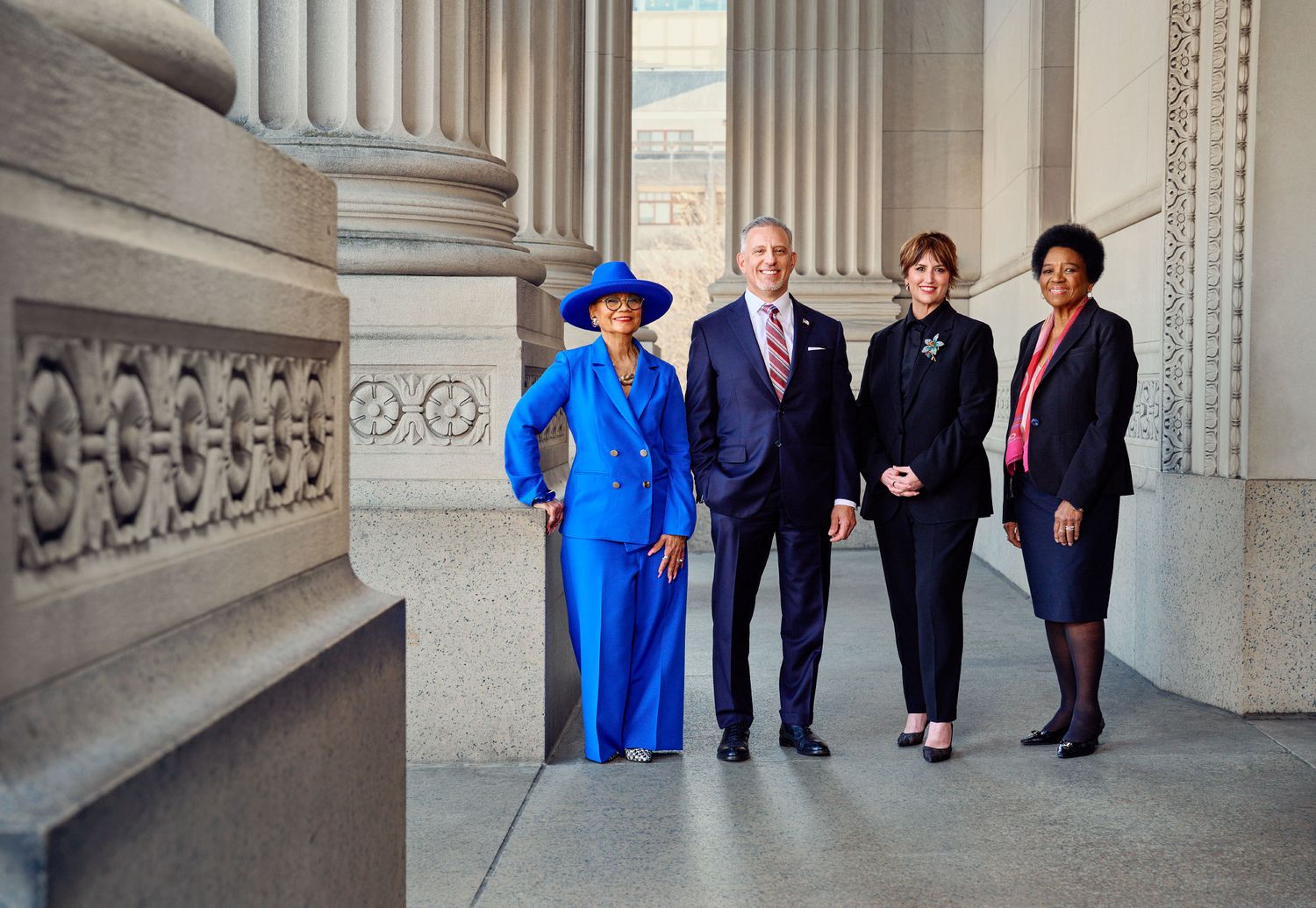 Four professionally dressed business leaders pose together on grand building steps.