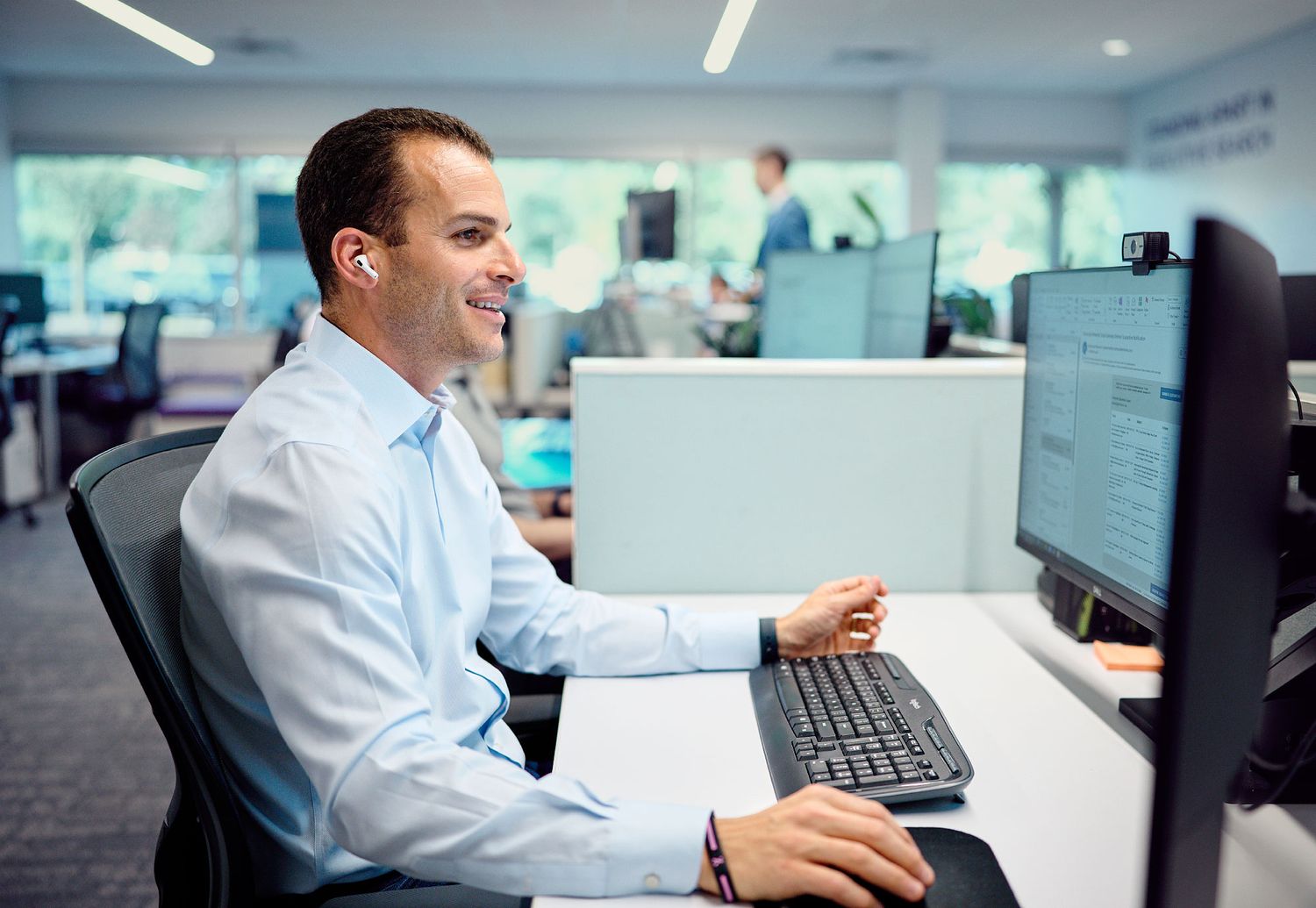 Smiling businessman working at computer desk in bright open-plan office environment.