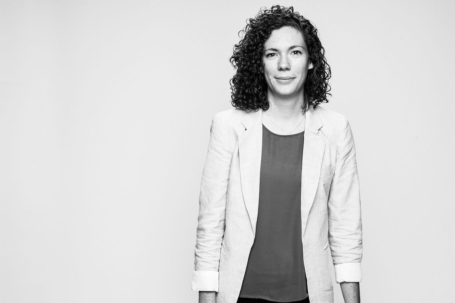 Black and white portrait of a curly-haired woman in a white blazer smiling confidently.