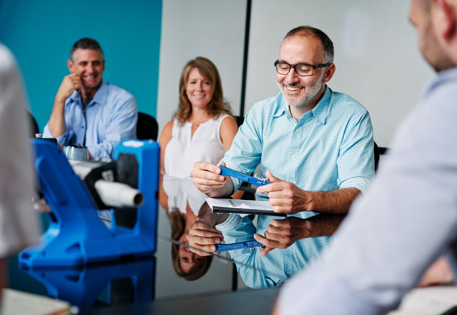 Business professionals smiling and collaborating during a modern office meeting around a reflective conference table.