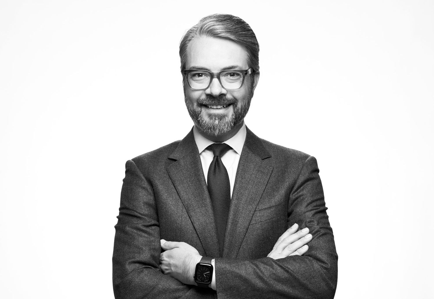 Professional man in suit and tie with beard standing with arms crossed on white background.