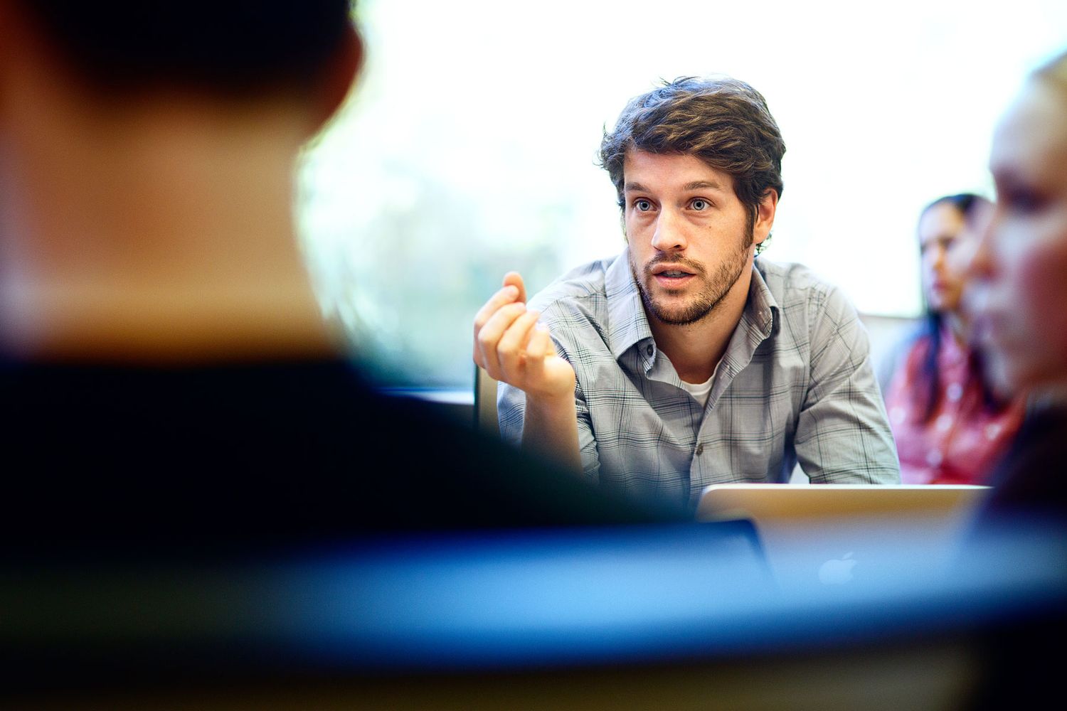 Young man gesturing while speaking during a group discussion or meeting in a casual indoor setting.