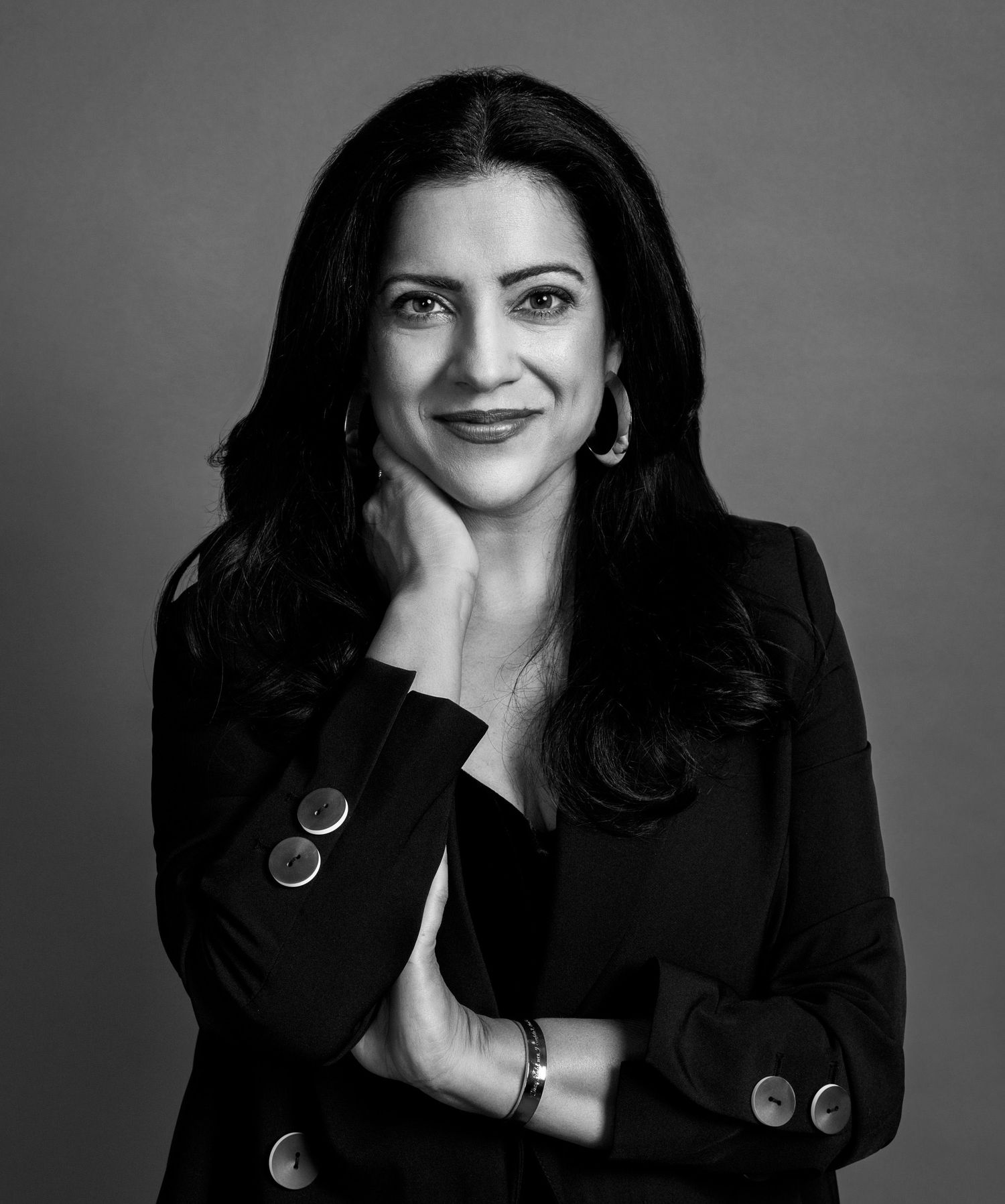 Professional black and white portrait of a confident woman in a blazer, smiling with hand on chin.