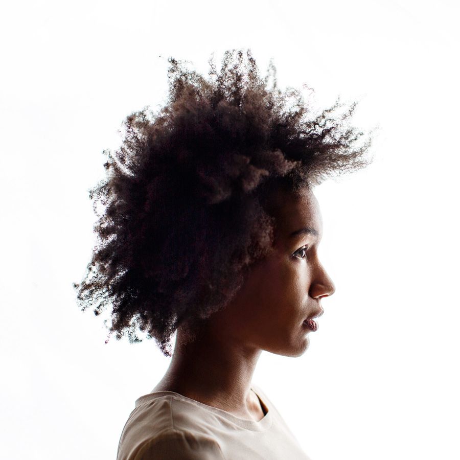 Profile view of a young woman with natural afro hair against a white background.