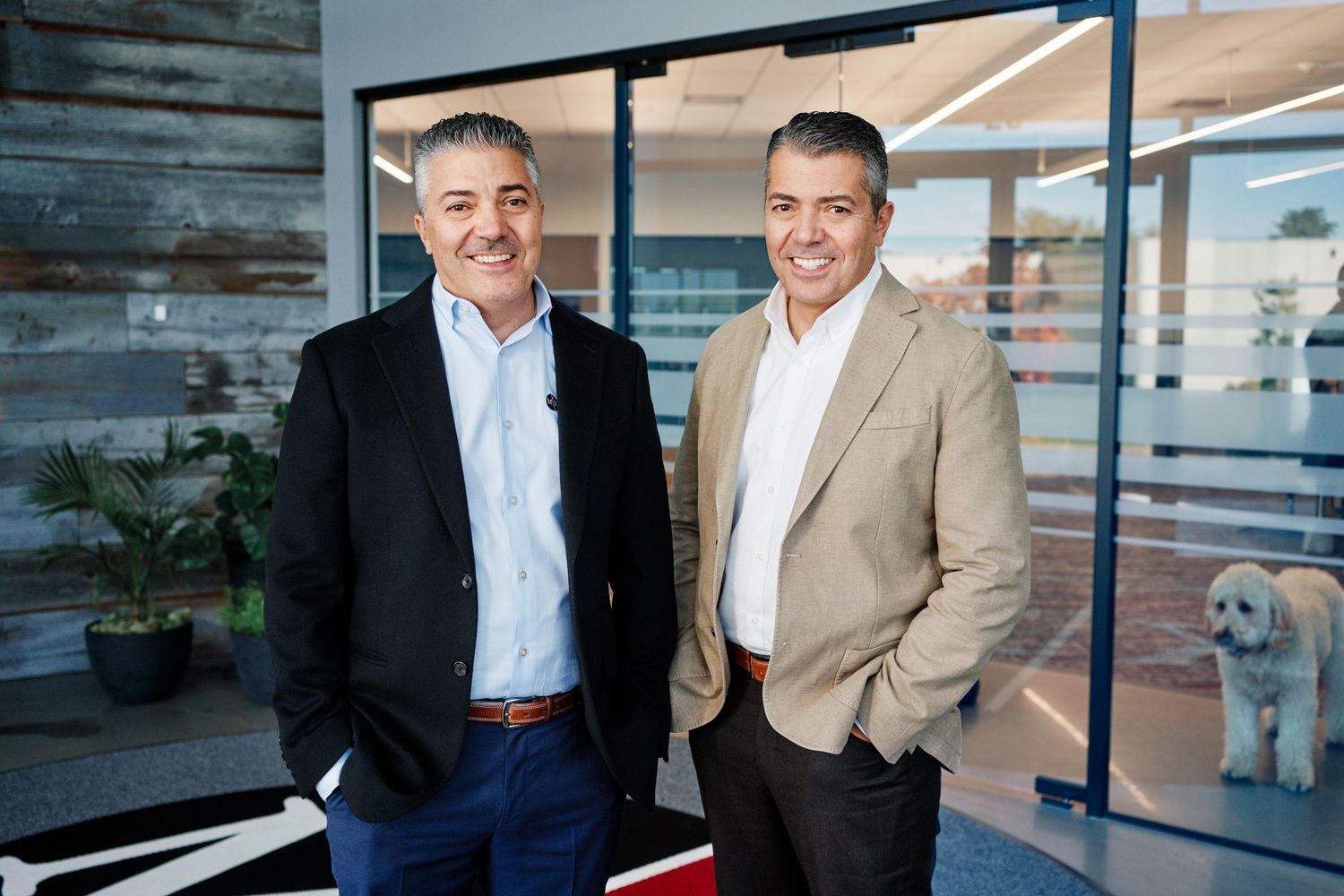 Two smiling business executives standing in modern office lobby with dog in background.