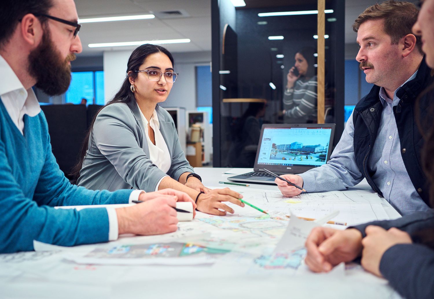 Three professionals reviewing maps and discussing project plans around a conference table in modern office.