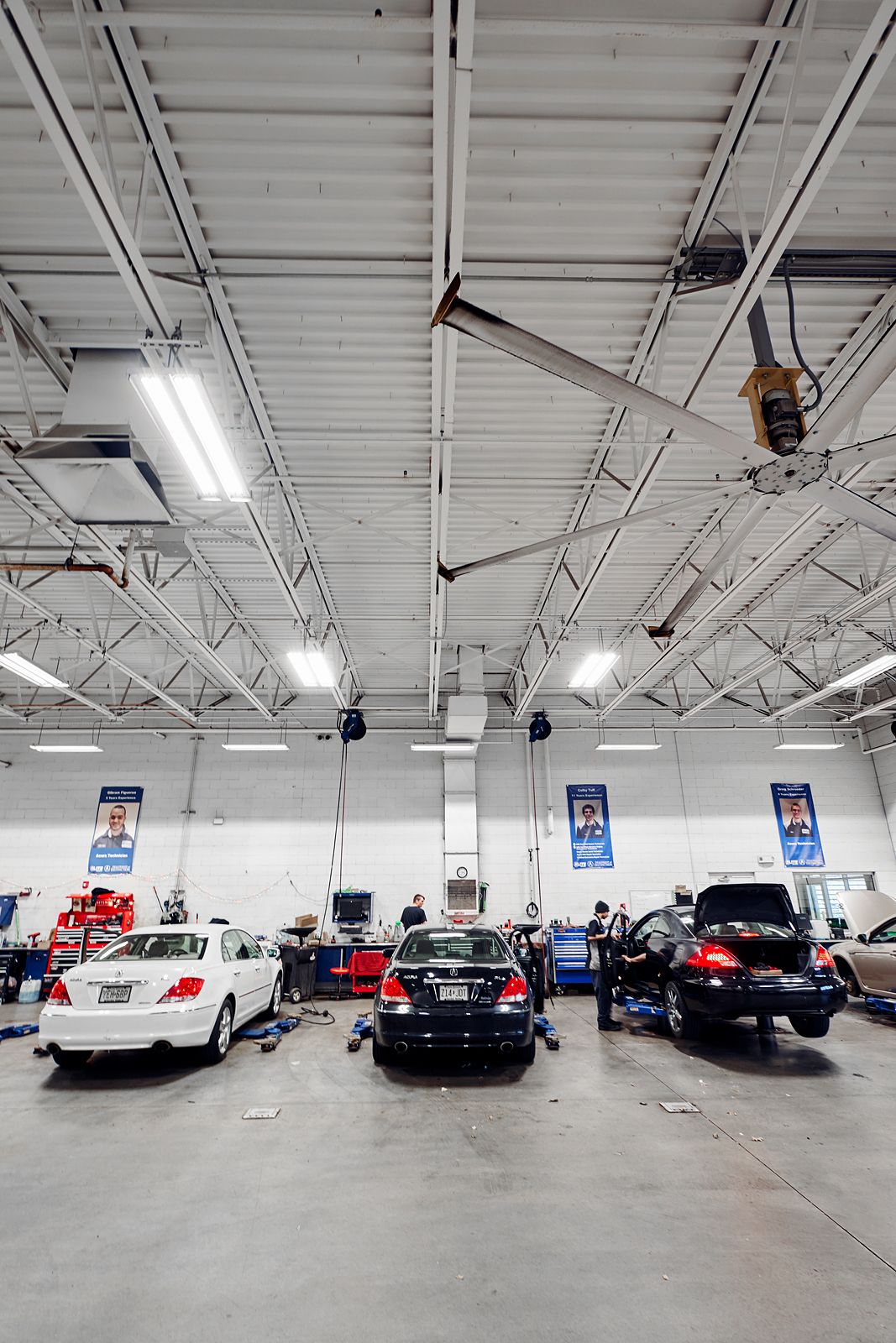 Cars being serviced in a large, well-lit auto repair shop with mechanics working and blue banners on walls.