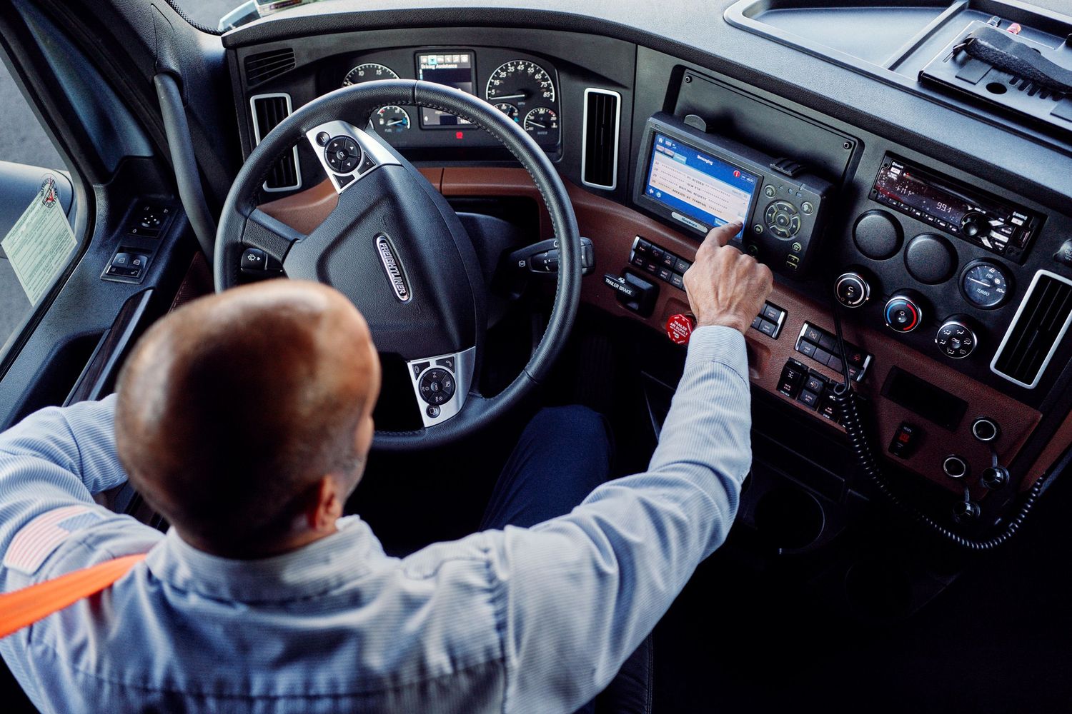 Overhead view of truck driver operating controls inside modern semi-truck cab.