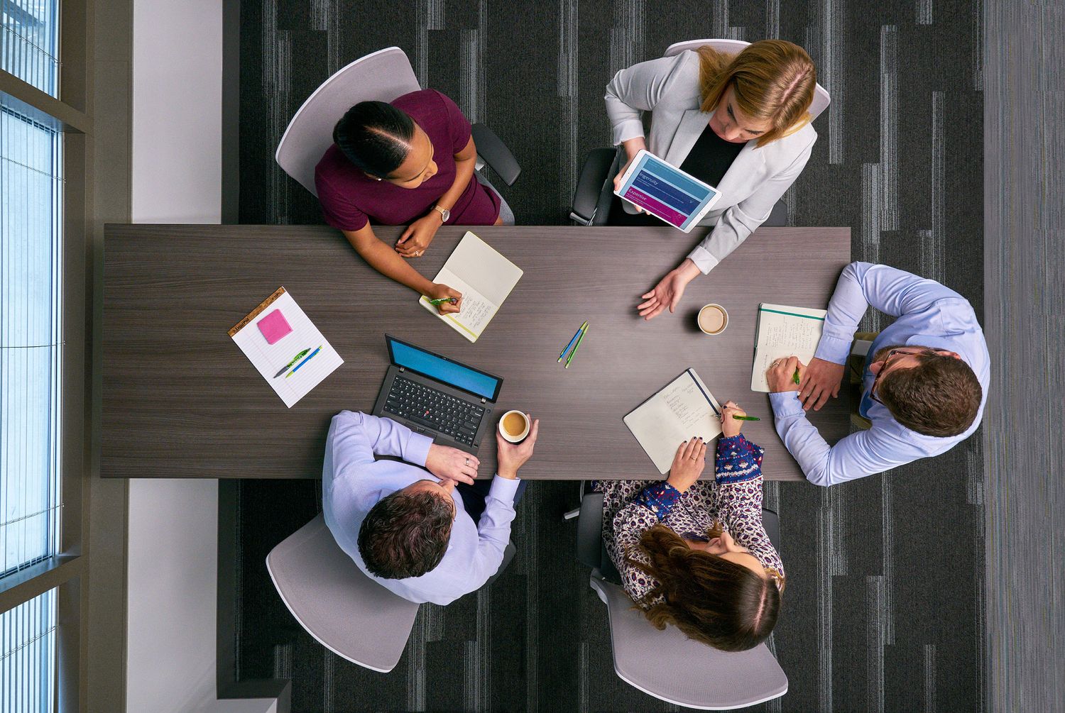 Overhead view of five business professionals collaborating around a conference table with laptops.