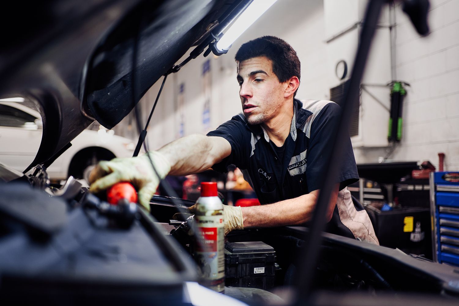 A mechanic works under the hood of a car in an auto repair shop, performing engine maintenance.