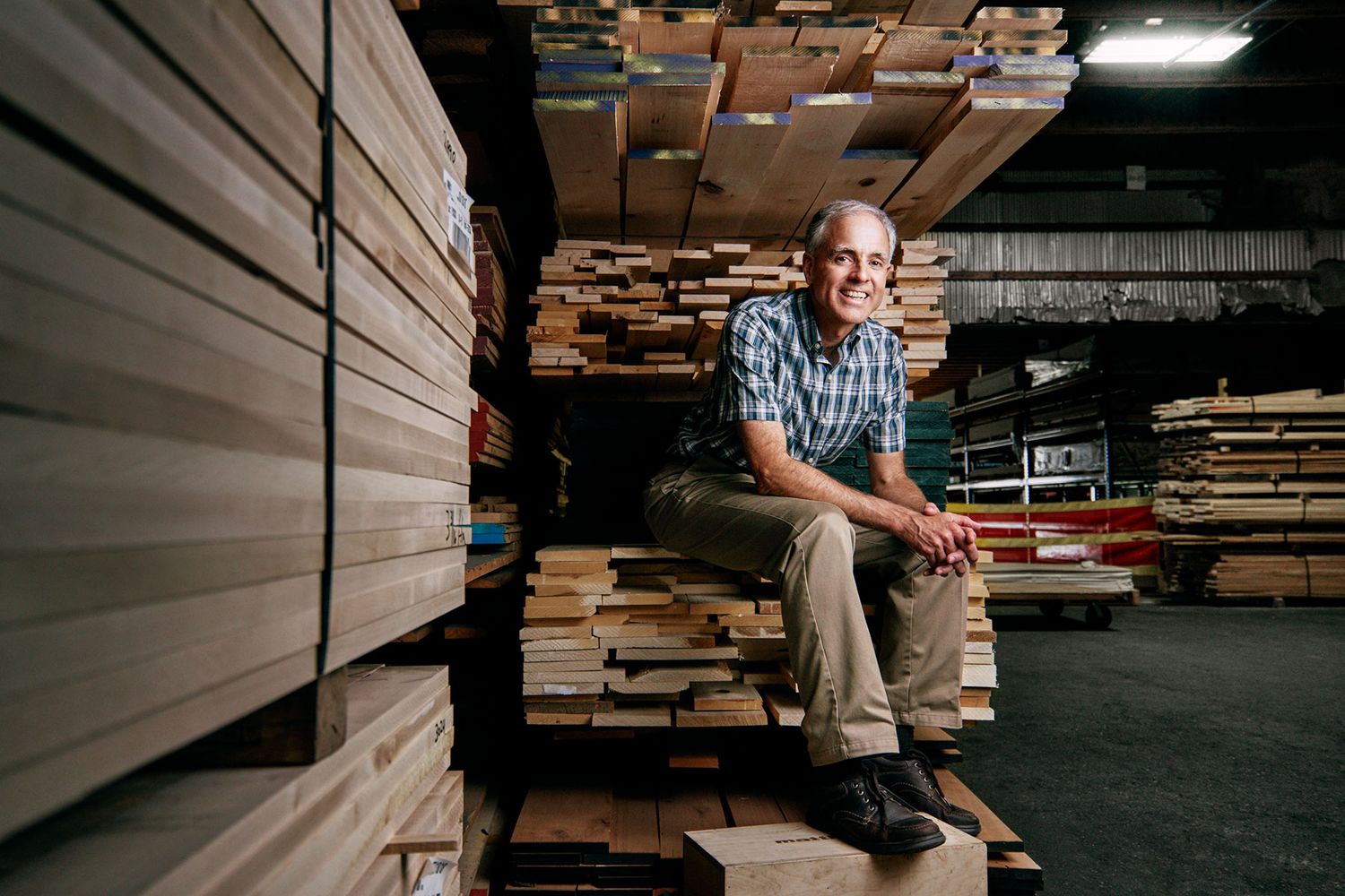 Man sitting on stacked lumber in a woodworking warehouse.