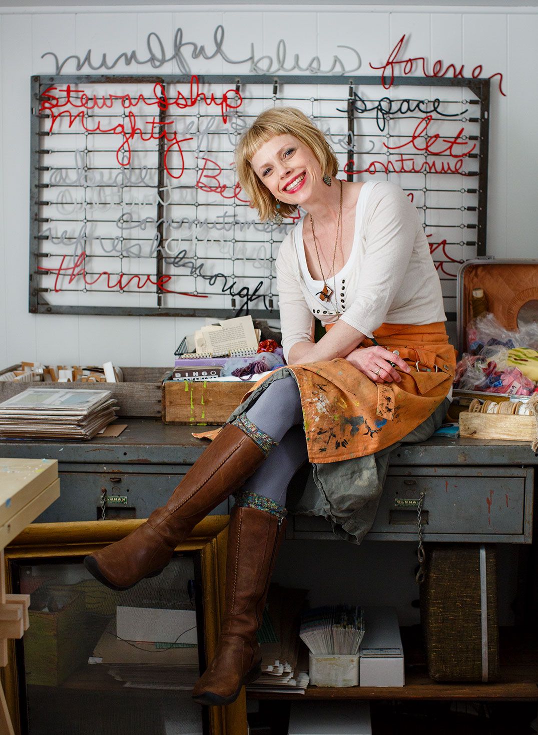 Creative woman sitting on desk in art studio with colorful word art installation on wall.
