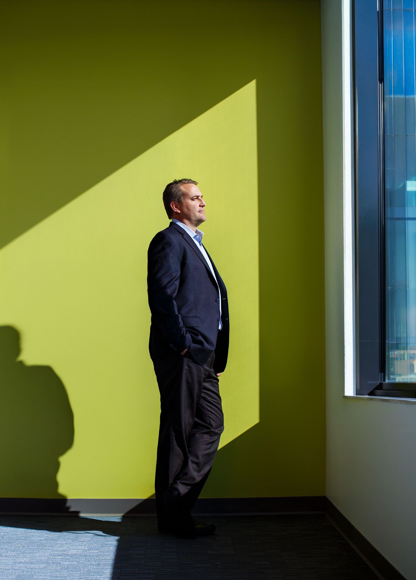 Man in suit standing against bright green wall with dramatic sunlight and shadow in modern office building.
