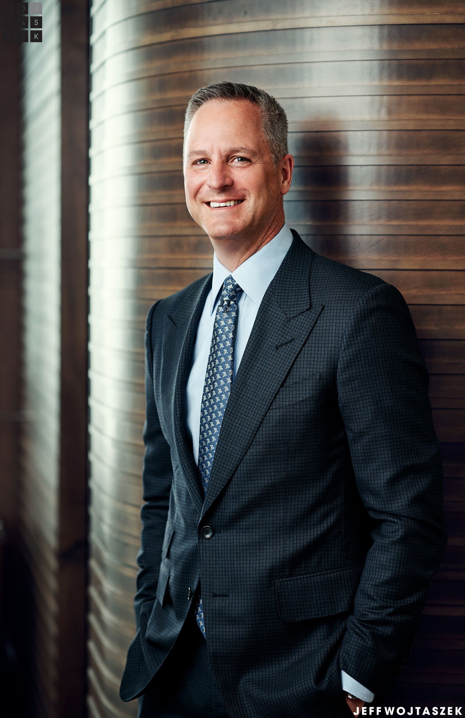Professional businessman in dark suit and tie smiling confidently in modern office setting, corporate portrait photography.