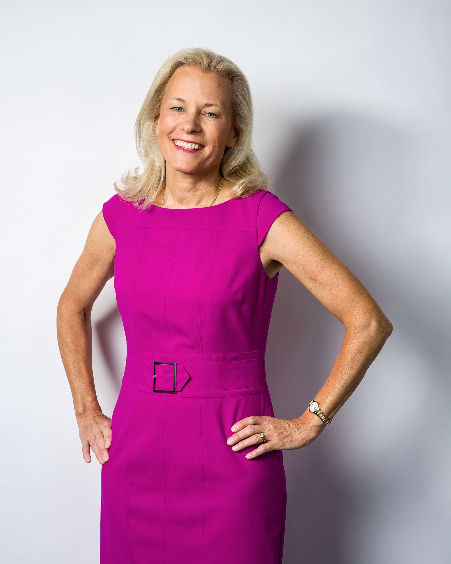 Confident woman in bright pink dress posing with hands on hips against white background.
