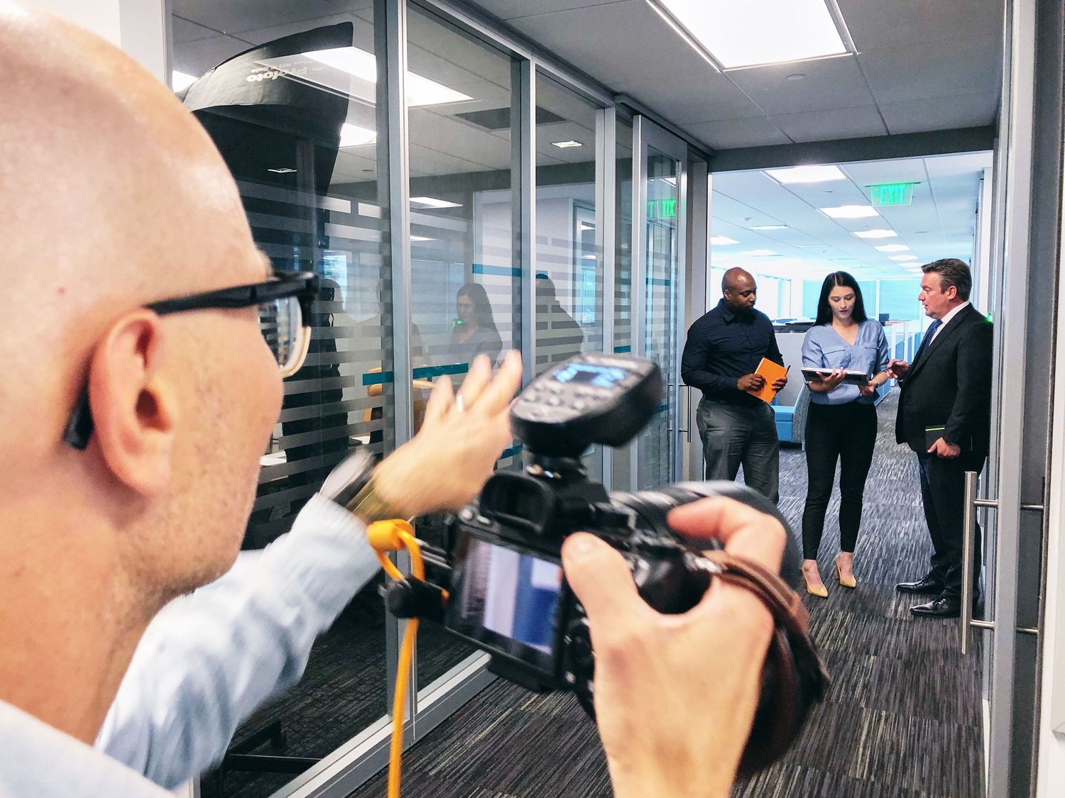Photographer capturing video of two professionals in a modern glass office during a corporate photoshoot.