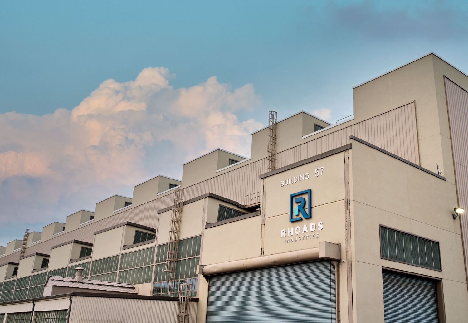 Exterior of Rhoads Industries building with white facade and logo signage under blue sky.