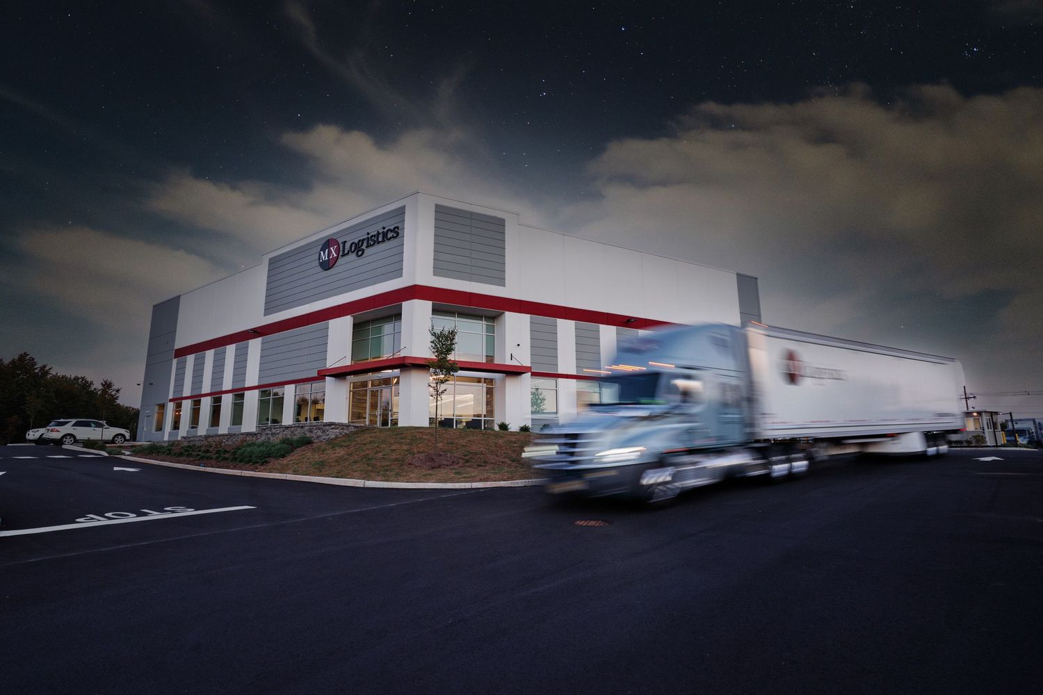 Syngenta distribution warehouse exterior at night with semi-truck driving past building.