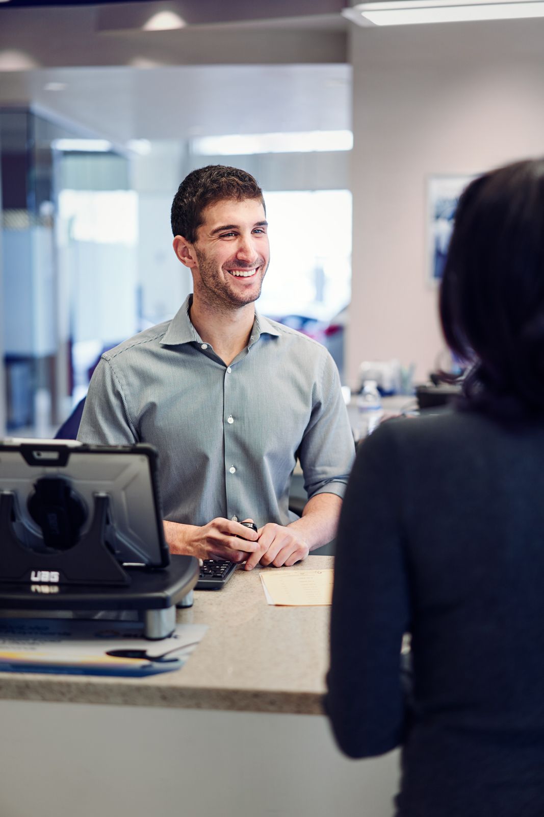 Smiling male receptionist assists a female customer at a modern service desk with a computer terminal.