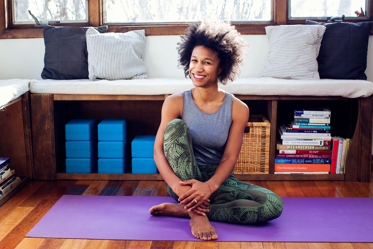 Smiling woman with natural hair sitting on purple yoga mat in home studio.