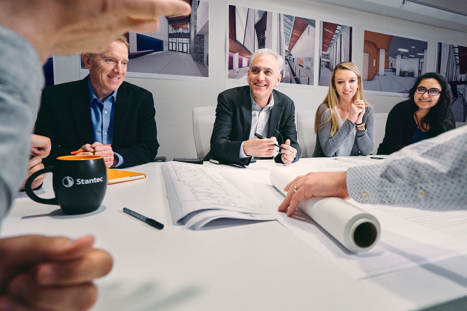 Professionals collaborate around a conference table reviewing architectural blueprints in a modern office meeting.