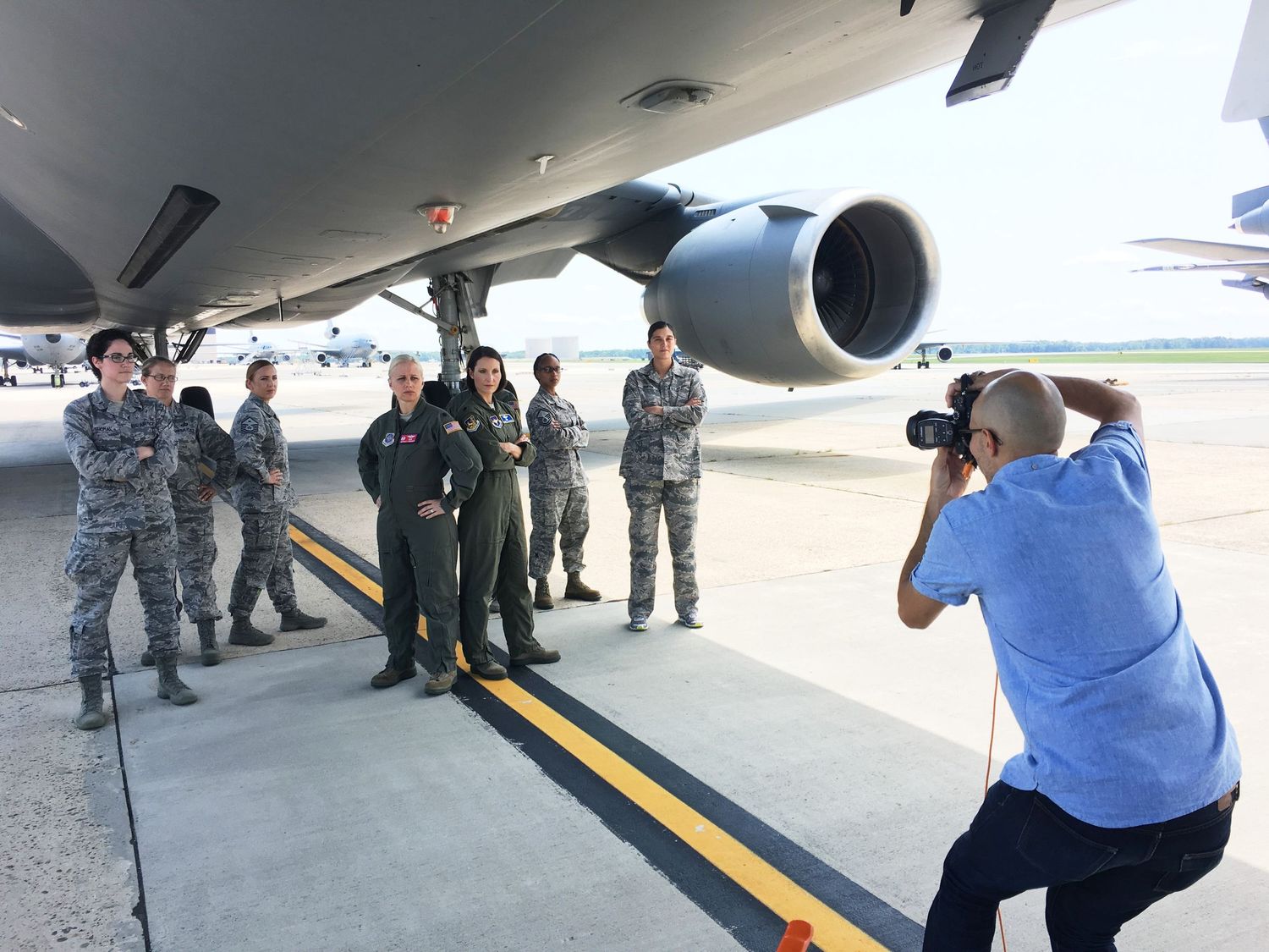 Photographer capturing a group of military personnel posing under a large aircraft engine.