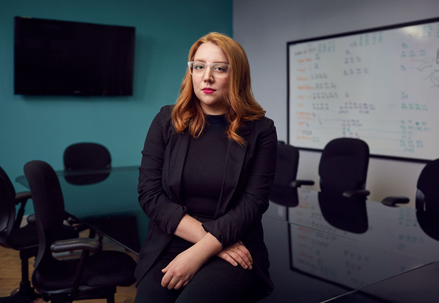 Young woman with red hair sitting in conference room with whiteboard.