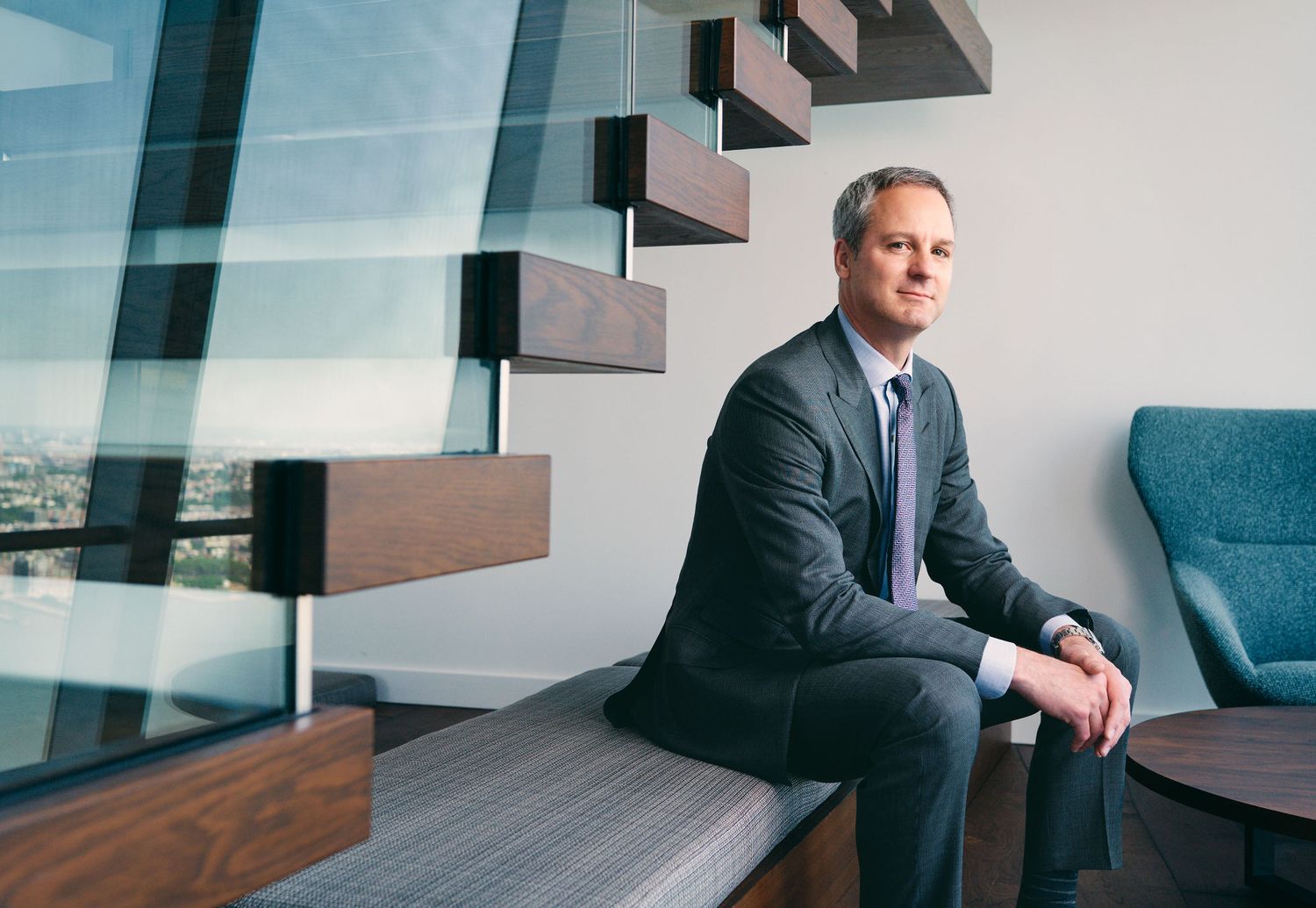 Professional businessman in gray suit sitting on bench in modern high-rise office space.