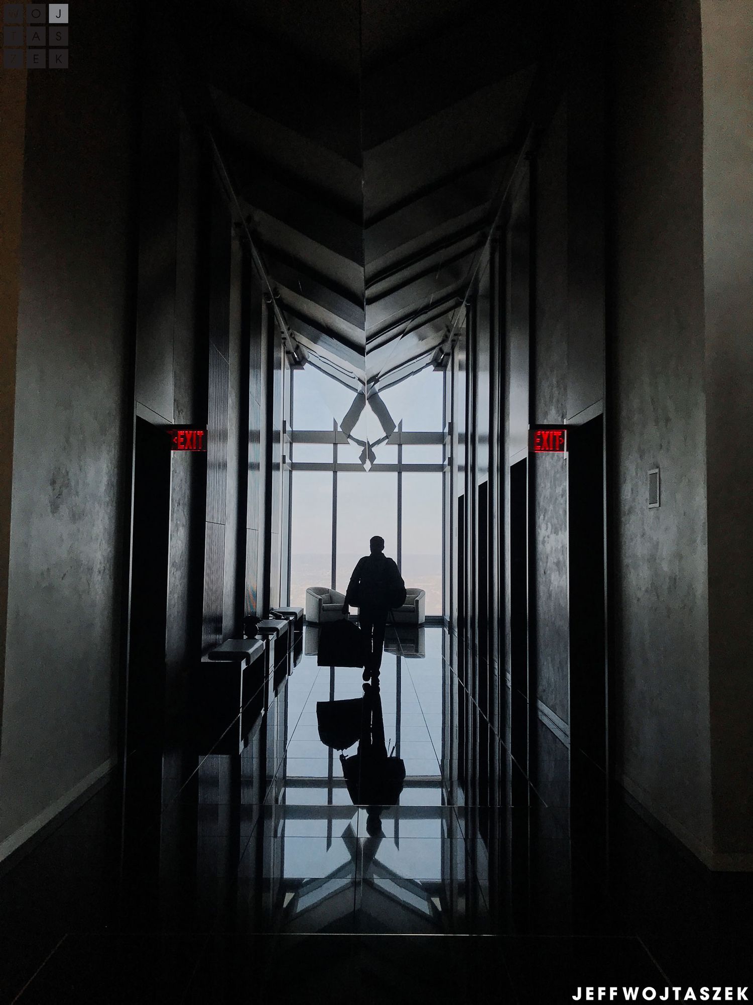 Silhouette of a person walking down a dark, elegant hotel corridor toward a large window with city views.