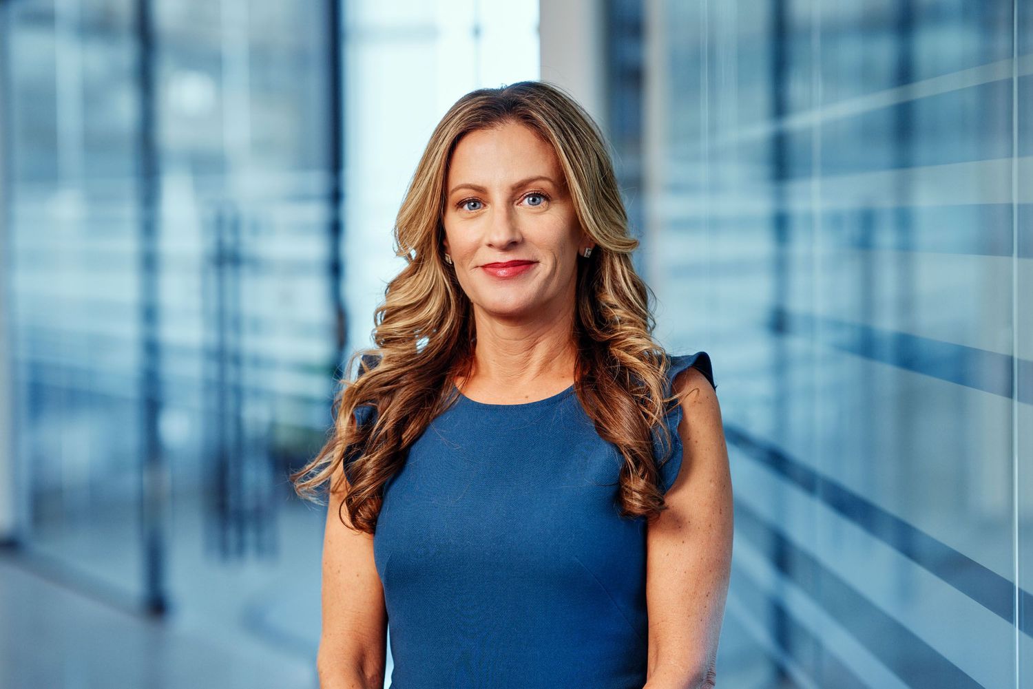 Professional businesswoman in blue dress poses confidently in modern corporate office.