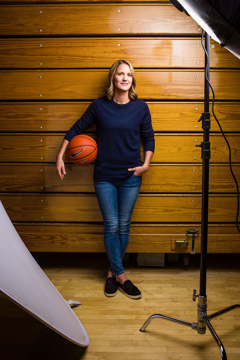 Woman in navy sweater holds basketball in gymnasium during professional photo shoot.