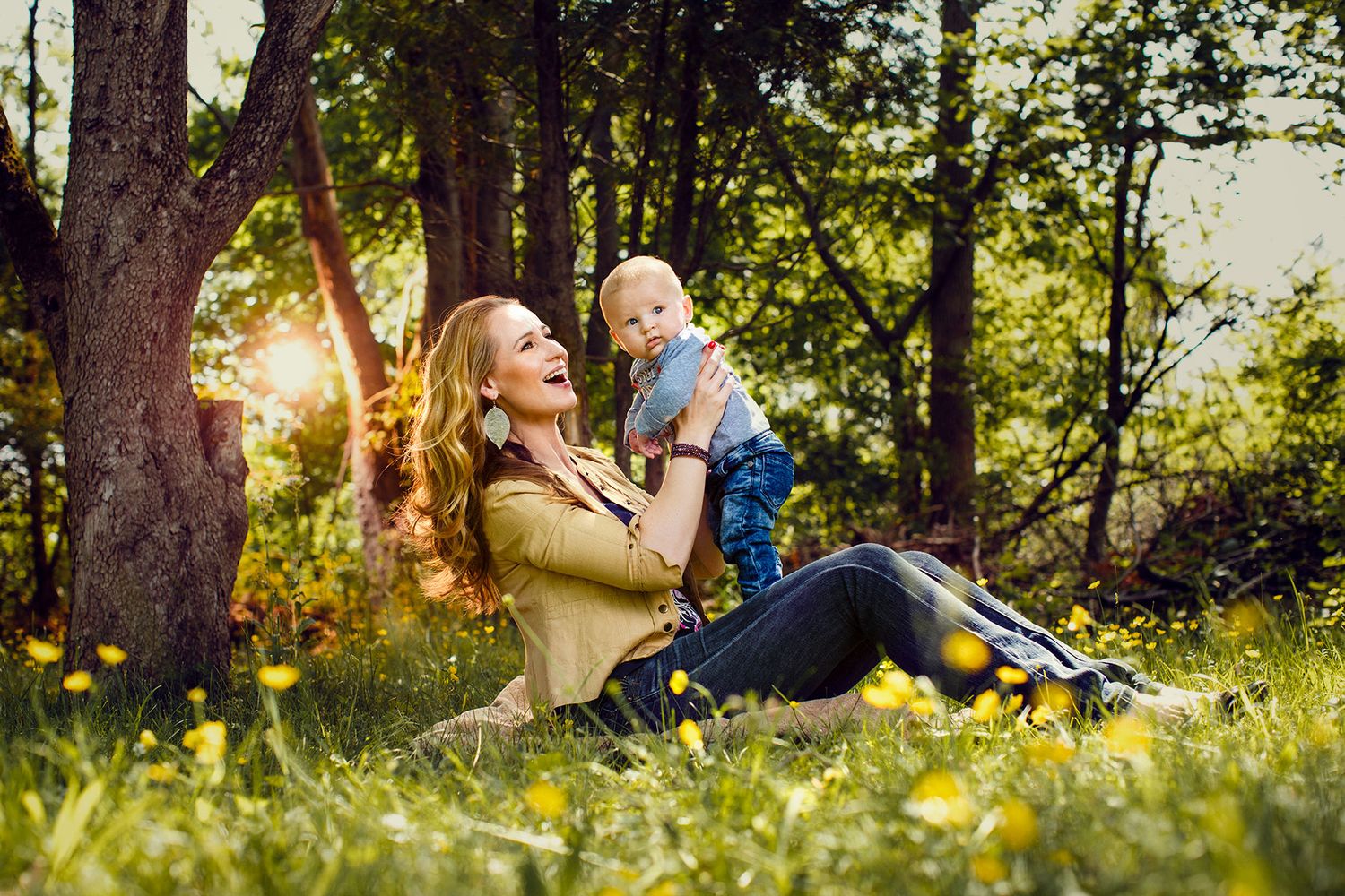 Happy mother playing with baby in a sunny green meadow.