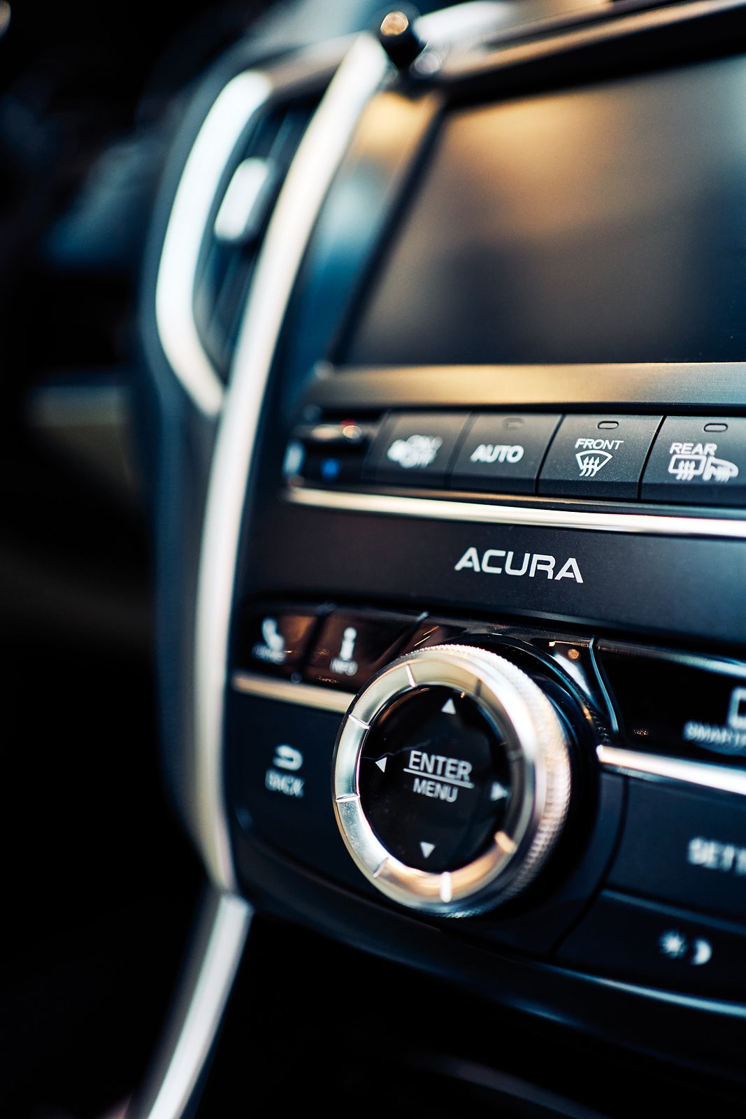Close-up of Acura car interior dashboard controls featuring climate and infotainment buttons with sleek chrome accents.