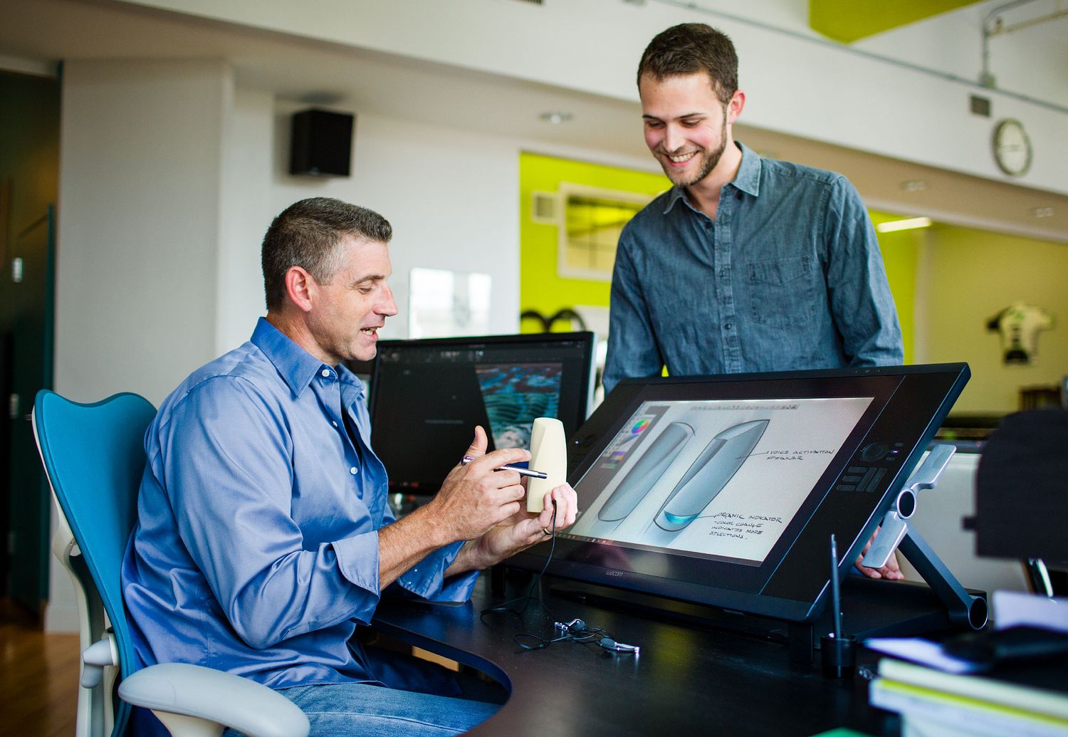 Two male colleagues collaborating on a product design using a digital drawing tablet in a creative office.