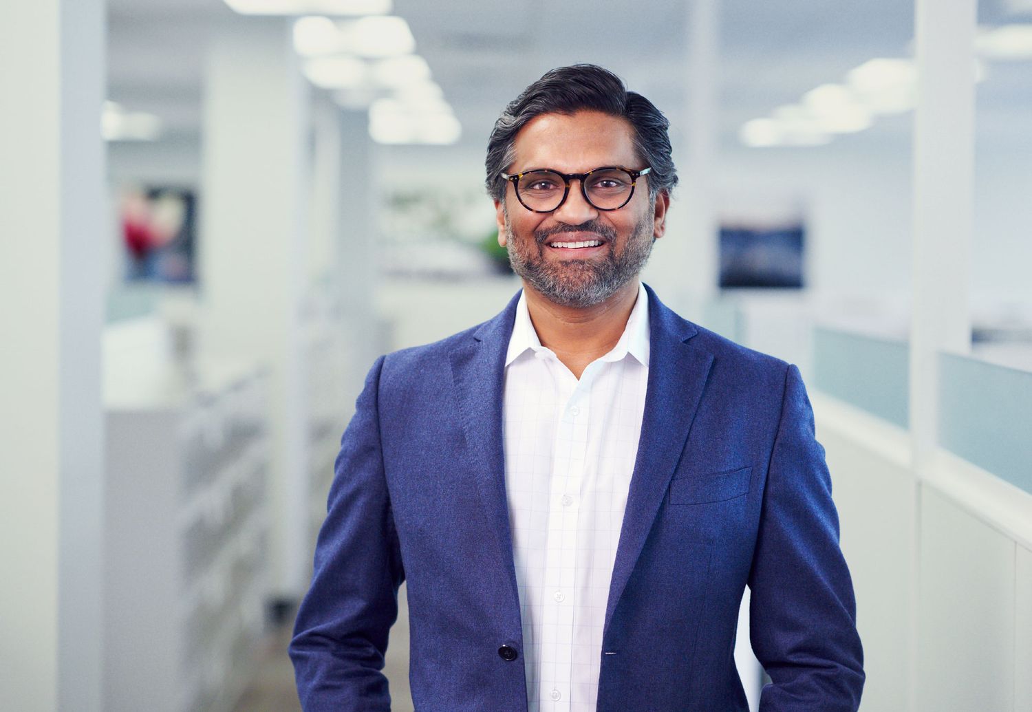 Smiling businessman in blue blazer standing in modern office corridor.
