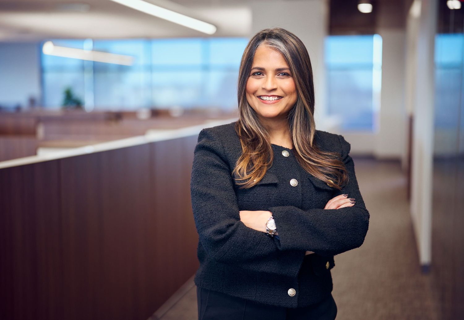 Confident businesswoman in black blazer stands with arms crossed in modern office environment.
