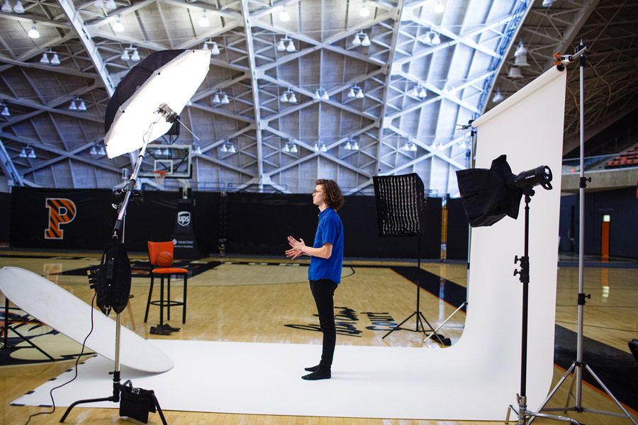 Person presenting in a professional photo studio setup inside a basketball gymnasium with lighting equipment and white backdrop.