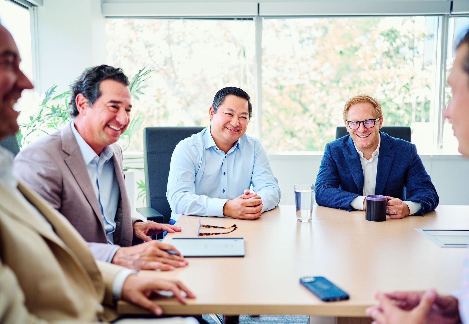 Diverse business professionals laughing and collaborating during a meeting in a modern conference room.