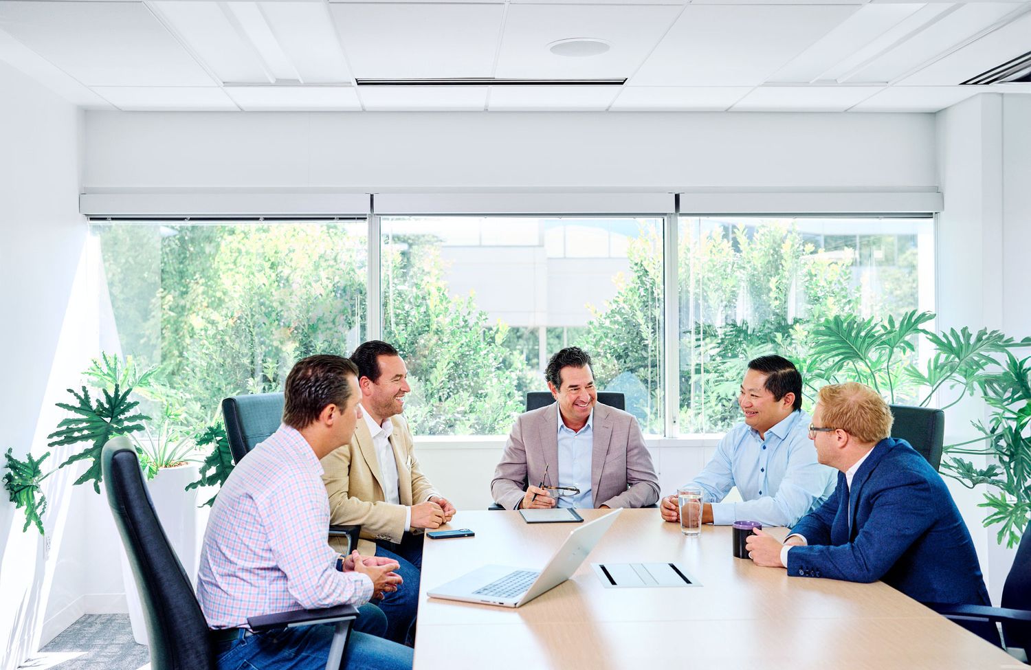 Five business professionals engaged in a collaborative meeting around a conference table in a bright modern office.