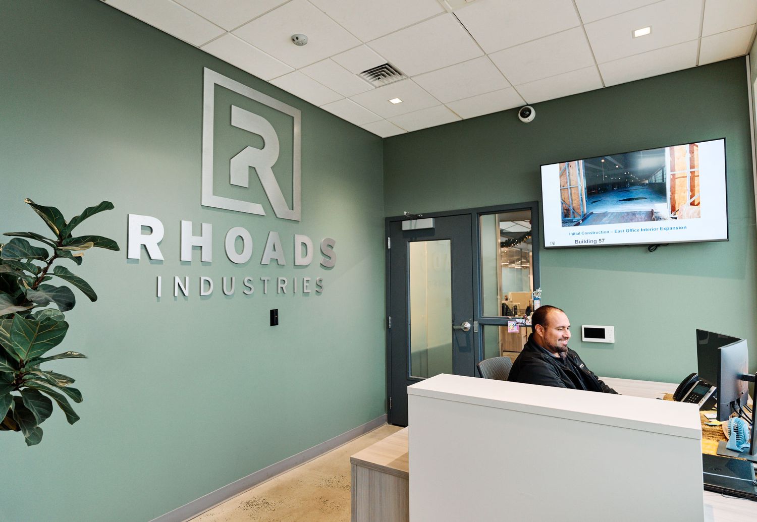 Modern Rhoads Industries reception desk with green accent wall and logo signage in corporate office.