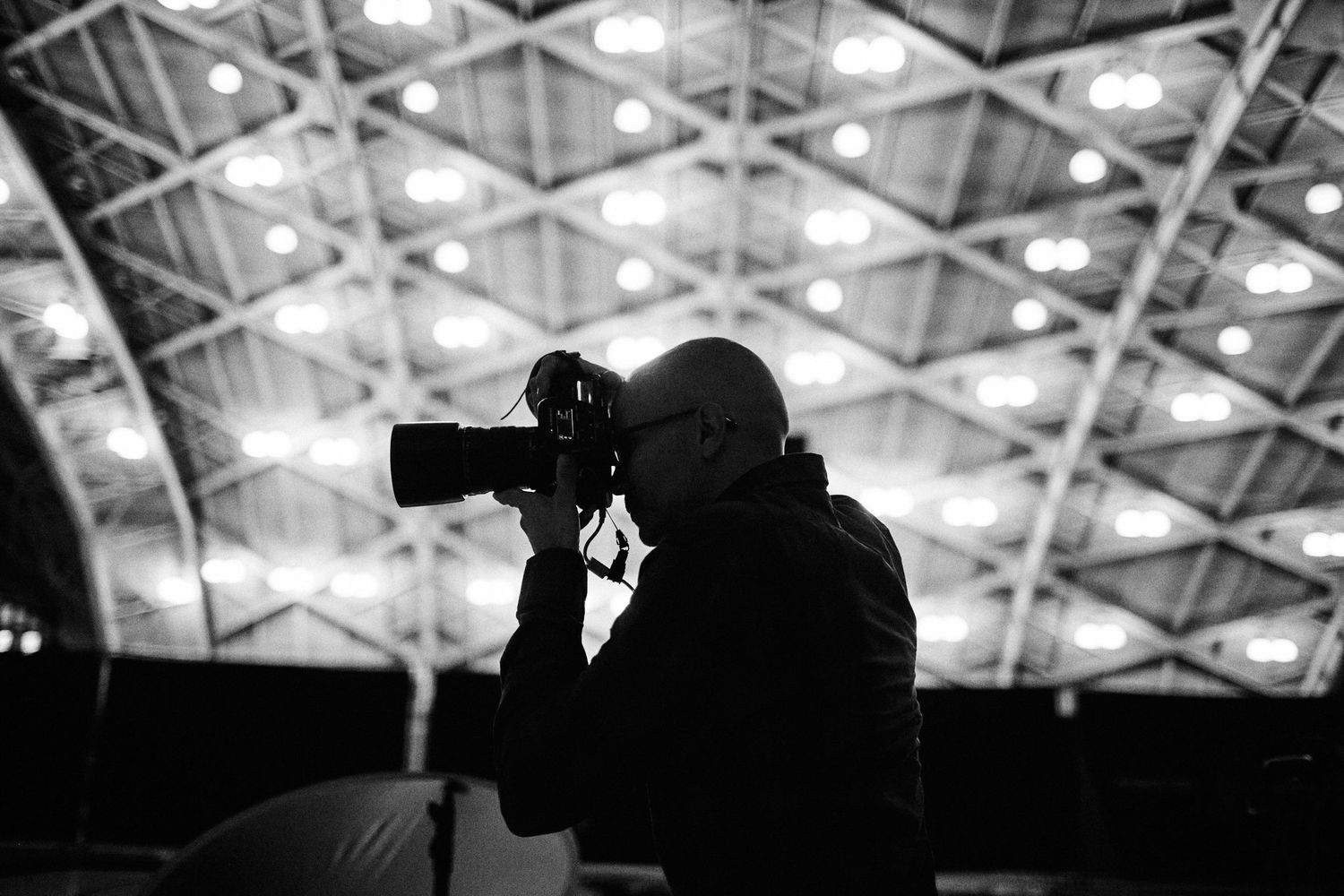 Black and white silhouette of photographer with camera under bright ceiling lights.