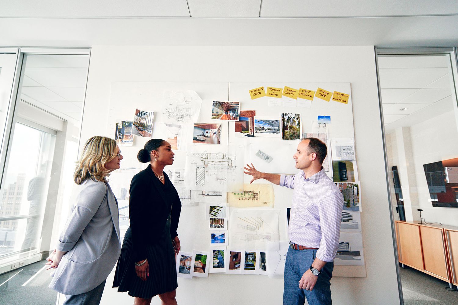 Three professionals reviewing design inspiration boards and sketches pinned to a white office wall.
