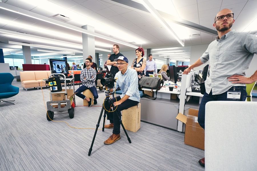 Film crew with cameras and equipment gathering in modern open-plan office space during production.