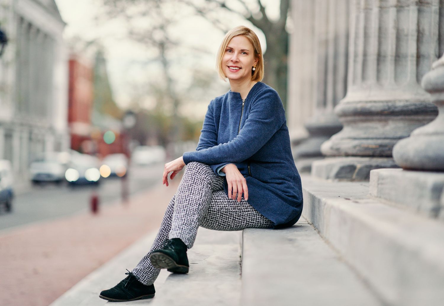 Casual woman in blue hoodie sitting on outdoor steps in urban setting.