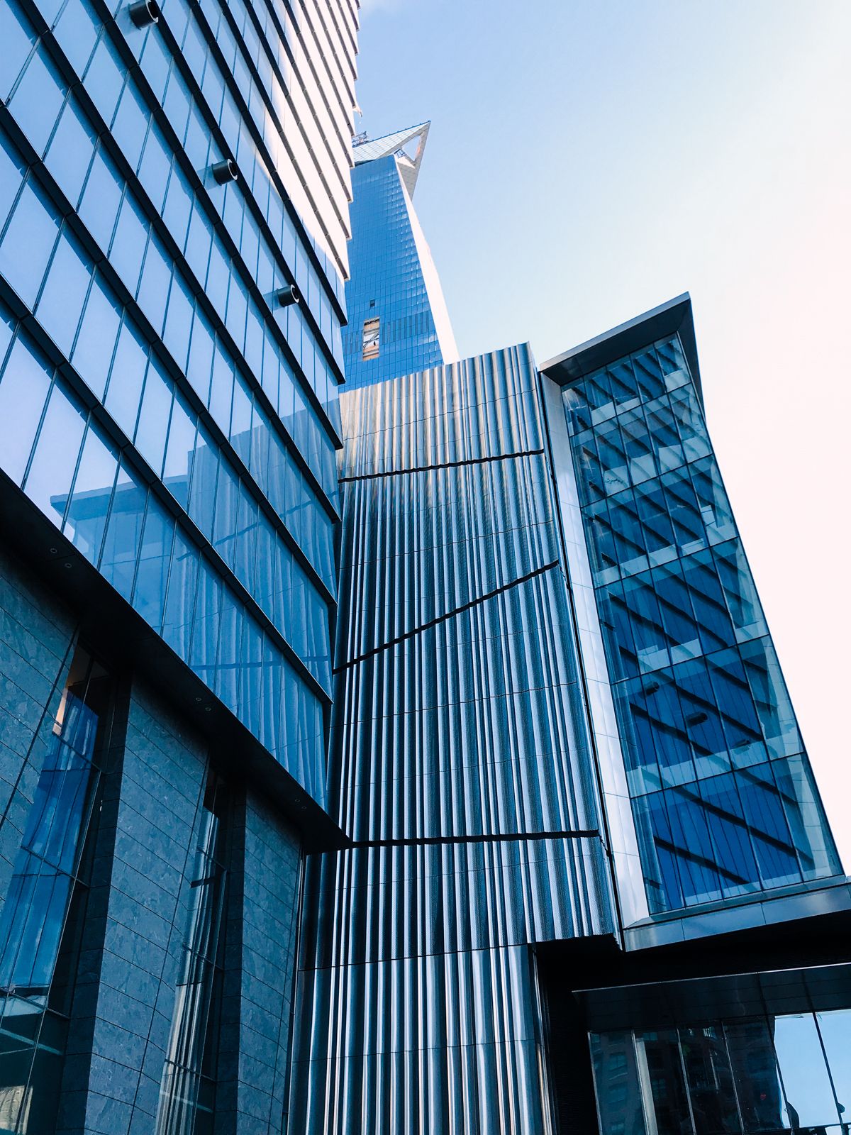 Modern glass skyscrapers tower against a clear blue sky, showcasing sleek architectural design with reflective facades.