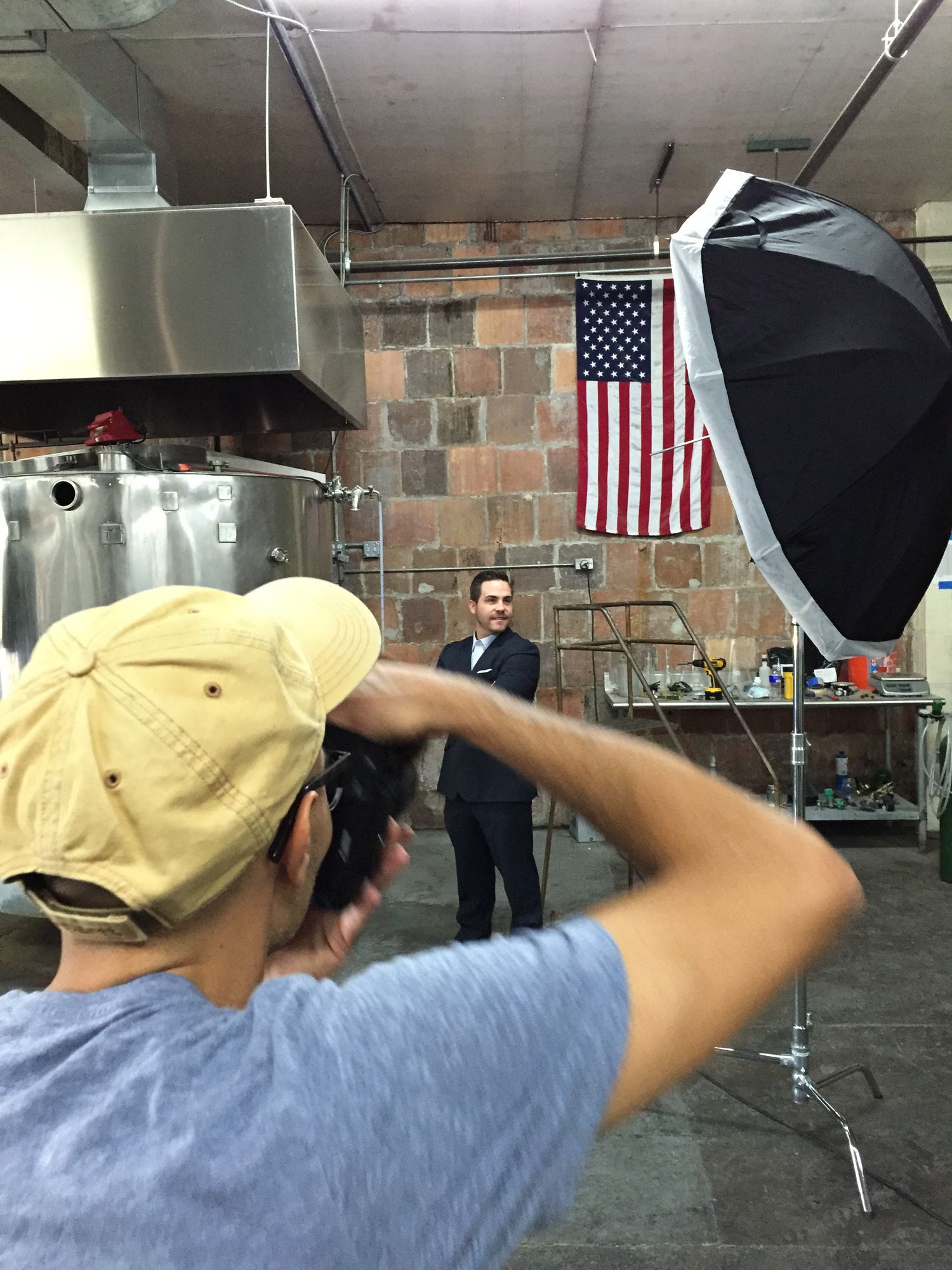 Photographer with softbox light photographing a man in a suit inside an industrial brewery space.