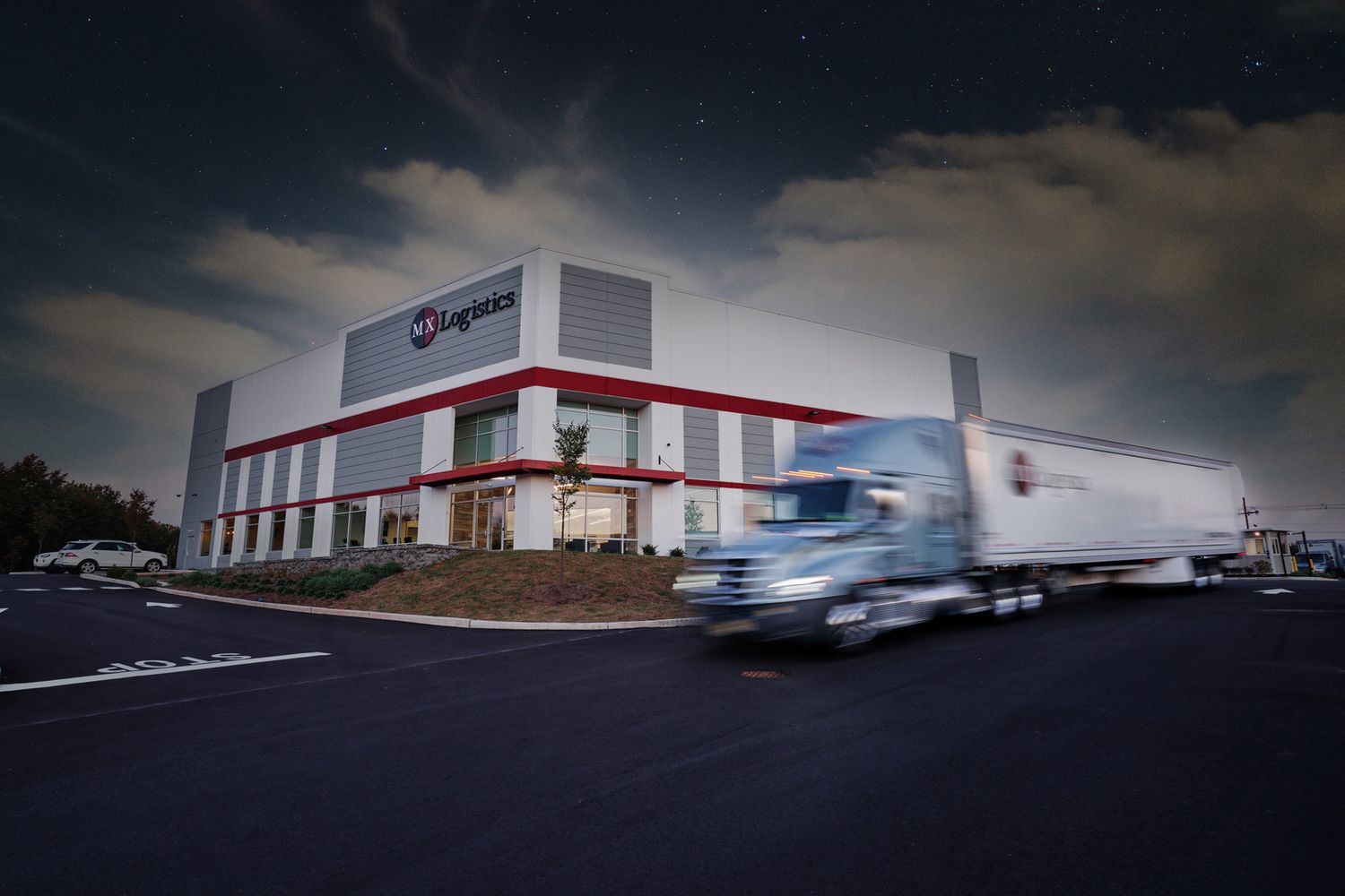 Rogan's distribution warehouse exterior at night with semi-truck in motion blur under dramatic sky.