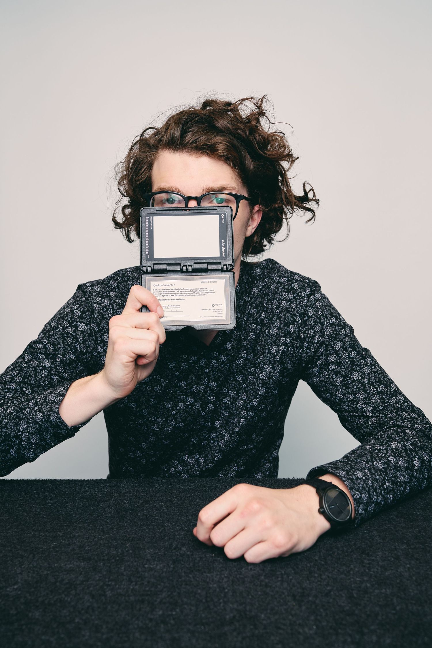 Man with curly hair and glasses holds a vintage electronic organizer in front of his face at a dark desk.