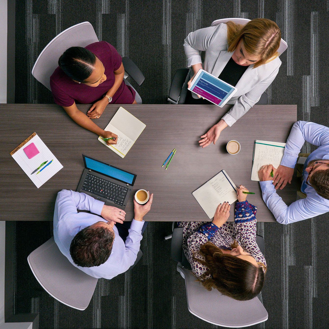 Overhead view of diverse business team collaborating at conference table with laptops, notebooks, and tablets.